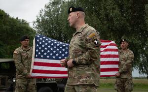 A U.S. soldier speaks in front of an American flag.