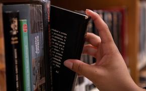 A close-up view of a hand taking a black-covered book from a library shelf.