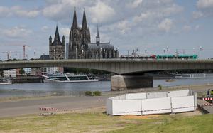 Cologne’s historic buildings seen in the background as a series of screens enclose an area by a river in the foreground.