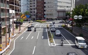 An overhead view of vehicles traveling through a city intersection with buildings in the background.